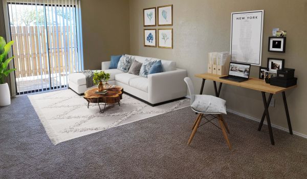 Living Oaks Apartments living room rendering with a large couch, coffee table, rug, desk, chair, wall art, and sliding glass doors leading to a private patio and letting natural light in