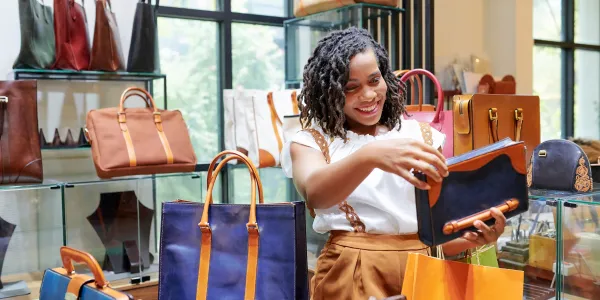 A smiling woman shopping at a department store and looking at purses and bags