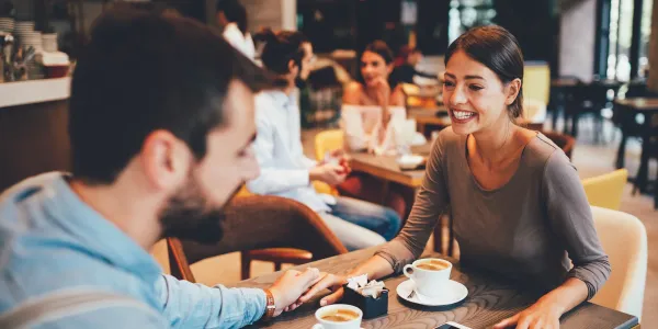 Man and woman with two espressos talking and holding hands at a coffee shop table